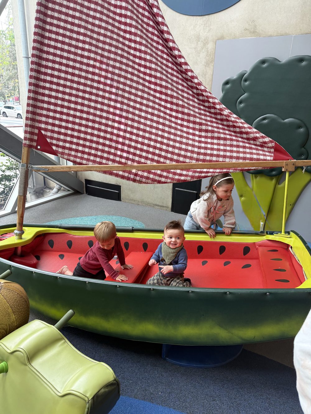 Children playing in a colorful watermelon sailboat at a play space
